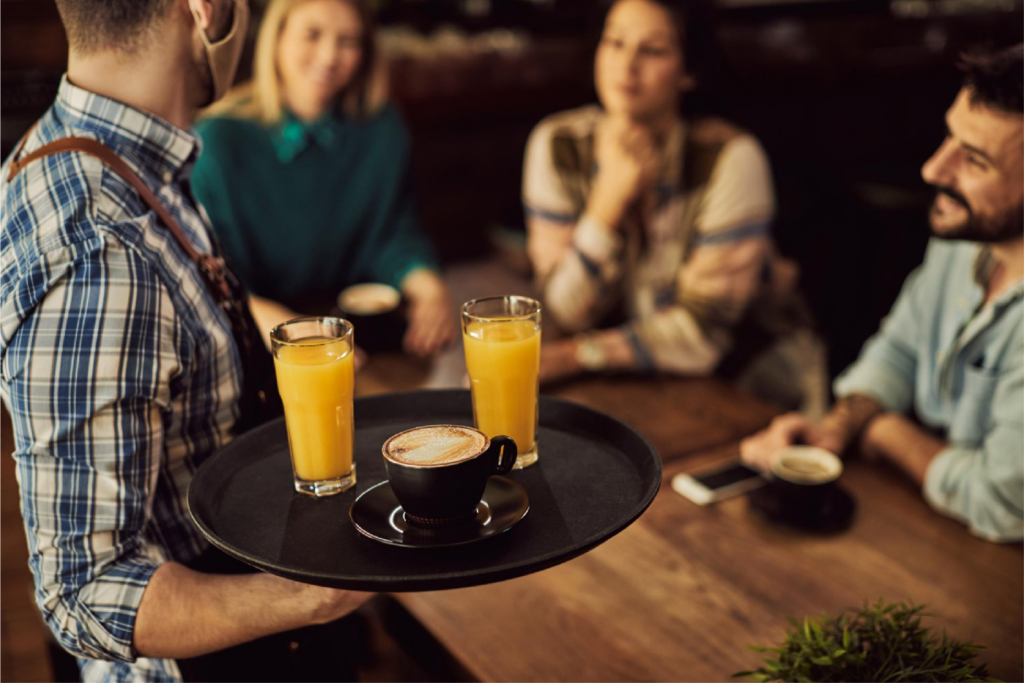 Camarero sirviendo con una bandeja a unas personas en una mesa de un bar